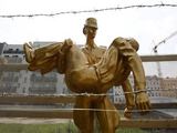 Reuters/Scanpix nuotr./Berlyno sienos memorialo skulptūra, vaizduojanti Rytų Vokietijos pasienietį, ianeaantį nuaauto Peterio Fechterio, mėginusio perlipti sieną, kūną