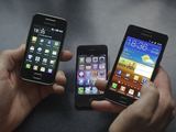 „Reuters“/„Scanpix“ nuotr./Vyras rankose laiko „Samsung Galaxy S II“ (d.) ir „Galaxy Ace“ išmaniuosius telefonus. Fone – „Apple“ telefonas „iPhone 4“.