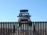 AFP/„Scanpix“ nuotr./Nuimamas ant 4,2 metrų aukščio tvoros, skiriančios Meksiką ir Ameriką, pakibęs kontrabandininkų džipas.